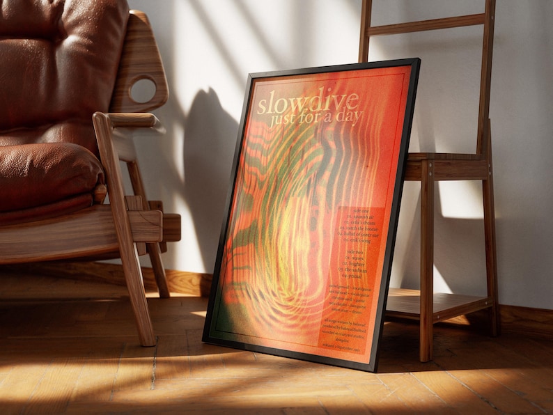 Może przedstawiać: Oprawiony plakat z napisem "slowdive just for a day" w czarnej ramie. Plakat ma czerwono-pomarańczowe tło z zielonymi i ż&oacute;łtymi falistymi liniami. Drewniane krzesło i drewniana p&oacute;łka znajdują się w tle.