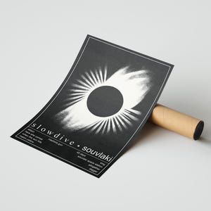 May include: A monochrome poster with the band name "slowdive" and album title "souvlaki". The design features a central dark circle with radiating white lines. It is propped against a brown cardboard tube.