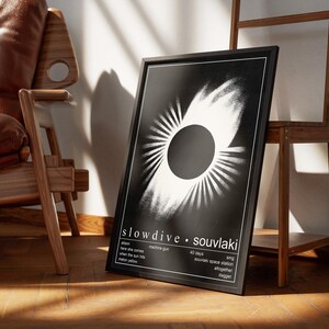 May include: A black framed poster displaying the "Souvlaki" album art by Slowdive. The monochrome design features a central circle with radiating lines. The poster includes the band's name and song titles.