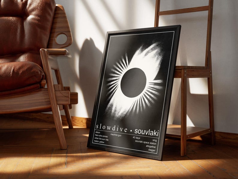 May include: A black framed poster displaying the "Souvlaki" album art by Slowdive. The monochrome design features a central circle with radiating lines. The poster includes the band's name and song titles.