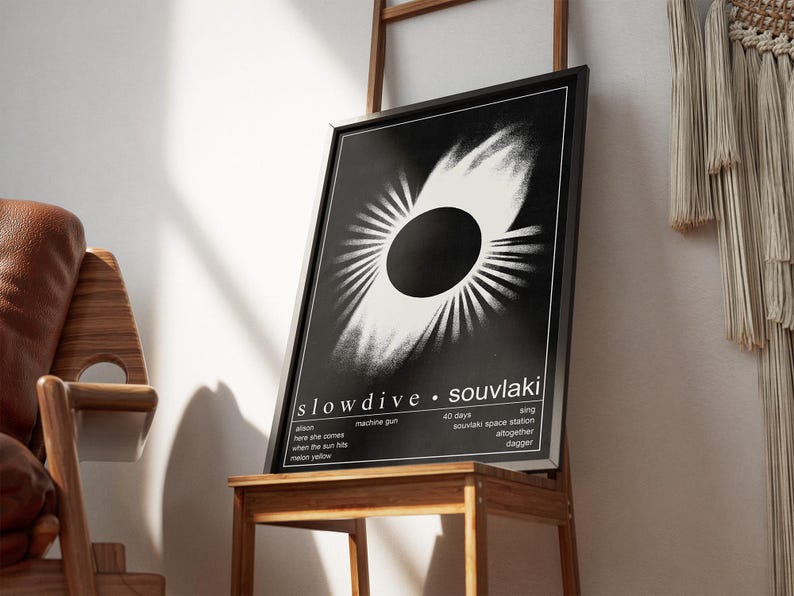 May include: A black framed art print with a white and black abstract design. The print, titled "slowdive souvlaki," is displayed on a wooden table. Song titles and lyrics are also printed on the artwork.
