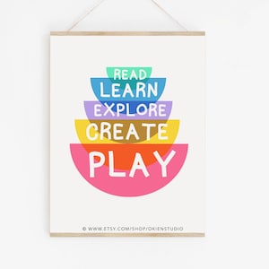 May include: A colorful print with the words "Read, Learn, Explore, Create, Play" arranged in a stack of rainbow-colored half-circles. The text is in white and the background is white.