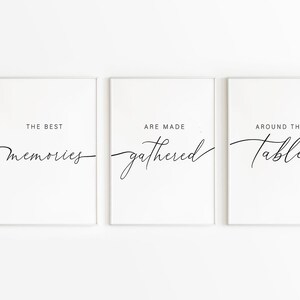 May include: Three framed wall art prints with a white background and black text. The prints read "THE BEST memories", "ARE MADE gathered", and "AROUND THE table" in a cursive font. The frames are white.