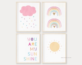 Puede incluir: Conjunto de cuatro impresiones de arte de pared imprimibles que presentan una nube rosa con gotas de lluvia, dos arcos iris con corazones, un sol y el texto "You Are My Sunshine" en letras de colores.