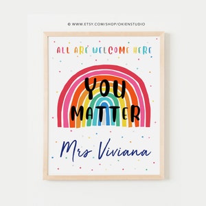 May include: A colorful rainbow with the words "You Matter" in black text. The rainbow is on a white background with small colorful dots. The text "All are welcome here" is at the top of the image and the text "Mrs. Viviana" is at the bottom of the image.