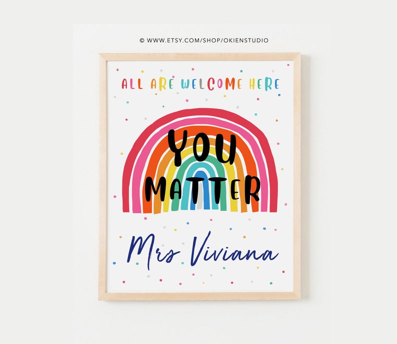 May include: A colorful rainbow with the words "You Matter" in black text. The rainbow is on a white background with small colorful dots. The text "All are welcome here" is at the top of the image and the text "Mrs. Viviana" is at the bottom of the image.