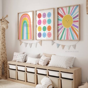 Könnte beinhalten: Drei bunte gerahmte Drucke mit einem Regenbogen, Smiley-Gesichtern und einer Sonne mit Strahlen. Die Drucke hängen an einer weißen Wand über einer Holzbank mit Aufbewahrungskisten. Die Bank ist mit Kissen dekoriert.