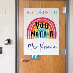 May include: A colorful rainbow with the words "You Matter" in black text and the words "All are welcome here" and "Mrs. Viviana" in blue text. The background is white with small colorful dots.