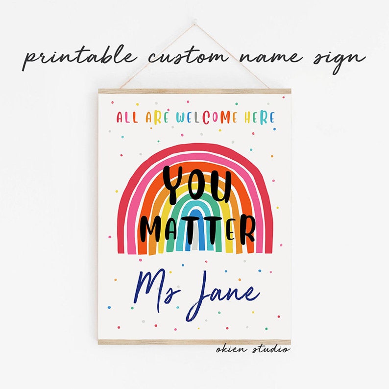 May include: Printable classroom sign with a rainbow and the text "You Matter" and "All are welcome here". The sign also includes the name "Ms. Jane" and the text "okien studio".