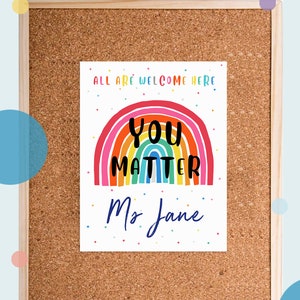 May include: A printable classroom poster with a rainbow and the text "All are welcome here. You matter. Ms. Jane". The background is a corkboard with colorful confetti.