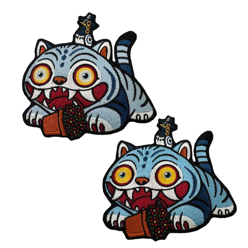 May include: Two embroidered patches featuring a cartoon tiger with a blue and white striped design. The tiger has large yellow eyes, a red open mouth, and is holding a small brown pot with red flowers. Each patch has a black hat.