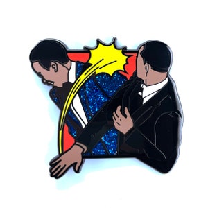 Puede incluir: Un pin de esmalte azul y negro que representa a dos hombres con traje. Un hombre está siendo empujado a través de una explosión de estilo cómic amarillo y rojo. El pin tiene un acabado azul brillante.