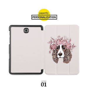 Pode incluir: Uma capa de tablet branca com um design floral que apresenta um cão usando uma coroa de flores. A capa está fechada e tem uma borda preta. O texto "papertify PERSONALIZATION" é visível na parte superior central da imagem.