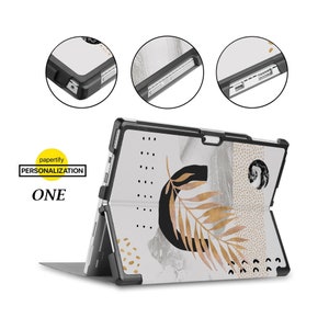 Könnte beinhalten: Eine weiße und graue Laptop-Hülle mit einem goldenen Blattdesign. Die Hülle hat einen schwarzen Rahmen und einen Ständer. Die Hülle ist geschlossen und der Bildschirm zeigt zur Kamera. Die Hülle trägt den Text "papertify PERSONALIZATION ONE" auf der Rückseite.