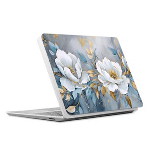 Op de afbeelding: Een witte laptop met een bloemenpatroon op de deksel. Het ontwerp bevat witte bloemen met gouden accenten op een blauwe en grijze achtergrond.