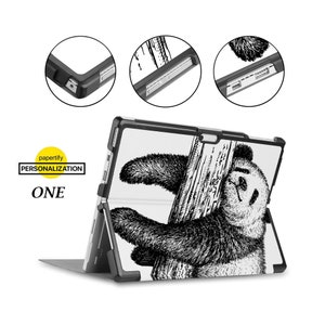 May include: Black and white illustration of a panda bear hanging from a tree branch. The illustration is printed on a white case for a Microsoft Surface tablet. The case is black and has a kickstand.