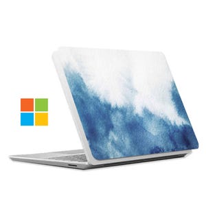 Puede incluir: Un ordenador portátil plateado con un diseño de acuarela blanco y azul en la tapa, que se asemeja a un cielo nublado o a olas del océano. El portátil tiene un logotipo de Microsoft.