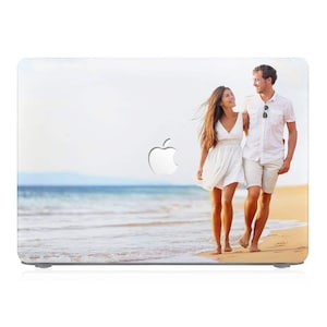 May include: A couple walk hand-in-hand on a sandy beach with blue water and a cloudy sky in the background. The woman is wearing a white dress and the man is wearing a white shirt and shorts.