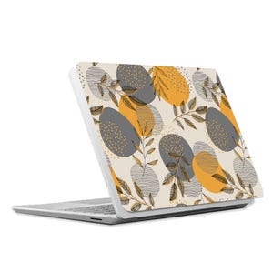May include: A white laptop with a patterned design on the lid. The pattern features gray and yellow circles with black leaf outlines on a cream background.