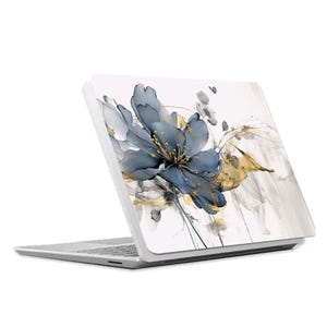 Op de afbeelding: Een witte laptop met een blauw en gouden bloemenontwerp op de achterkant. Het ontwerp toont een grote blauwe bloem met gouden accenten op een witte achtergrond.