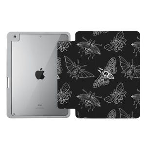 May include: A silver iPad in a protective case next to a black cover with a white insect pattern. The pattern features various stylized moths and beetles. The iPad is visible on the left, while the patterned cover is on the right.