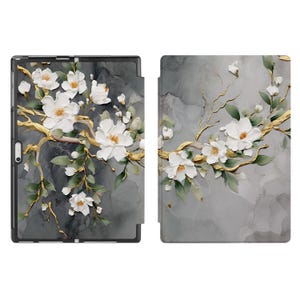 May include: A tablet case with a floral design. White flowers with yellow centres and green leaves are set against a grey background with gold-coloured branches. The case is shown open and closed, displaying the full design.