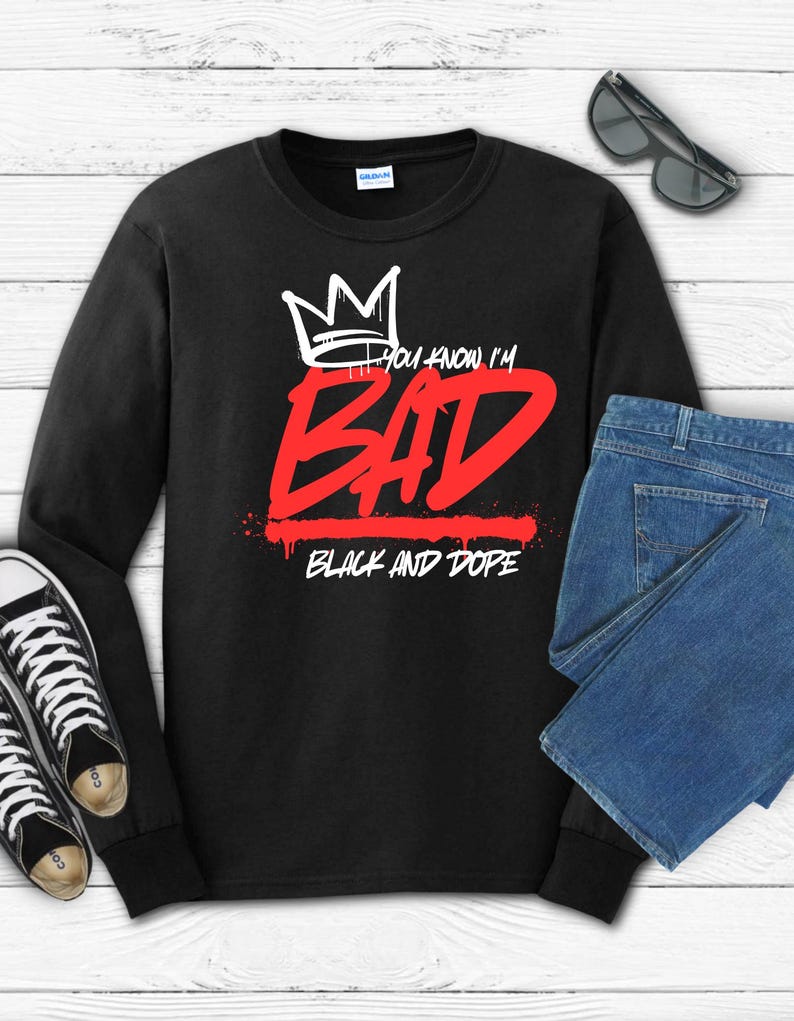 May include: Black long-sleeve sweatshirt with the text "You know I'm BAD" in red and white, and "BLACK AND DOPE" in white. The design includes a crown graphic. The image also shows black sunglasses, blue jeans, and black and white sneakers.