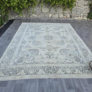 May include: A large rectangular area rug featuring a cream-colored base with intricate dark gray floral and geometric patterns. The design includes a central medallion surrounded by ornate botanical motifs and a wide decorative border.