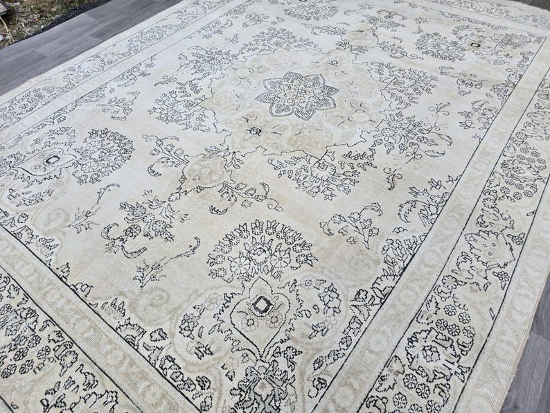 May include: A large rectangular area rug featuring a cream-colored background with intricate black line-drawn floral and geometric patterns. The design includes a central medallion surrounded by symmetrical botanical motifs and a wide decorative border.
