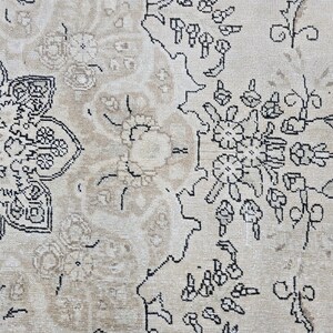 May include: A woven rug featuring a light beige background with intricate black line-drawn floral and geometric patterns. The design includes a large, detailed central medallion motif on the left side and smaller floral clusters on the right.