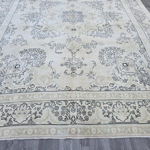 May include: A large rectangular area rug featuring a cream-colored background with intricate black floral and vine patterns. The design includes a central medallion surrounded by symmetrical botanical motifs and a wide decorative border.