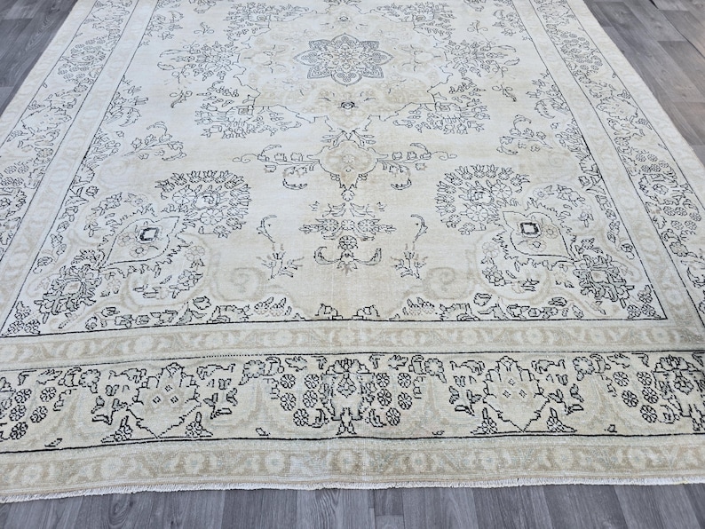 May include: A large rectangular area rug featuring a cream-colored background with intricate black floral and vine patterns. The design includes a central medallion surrounded by symmetrical botanical motifs and a wide decorative border.