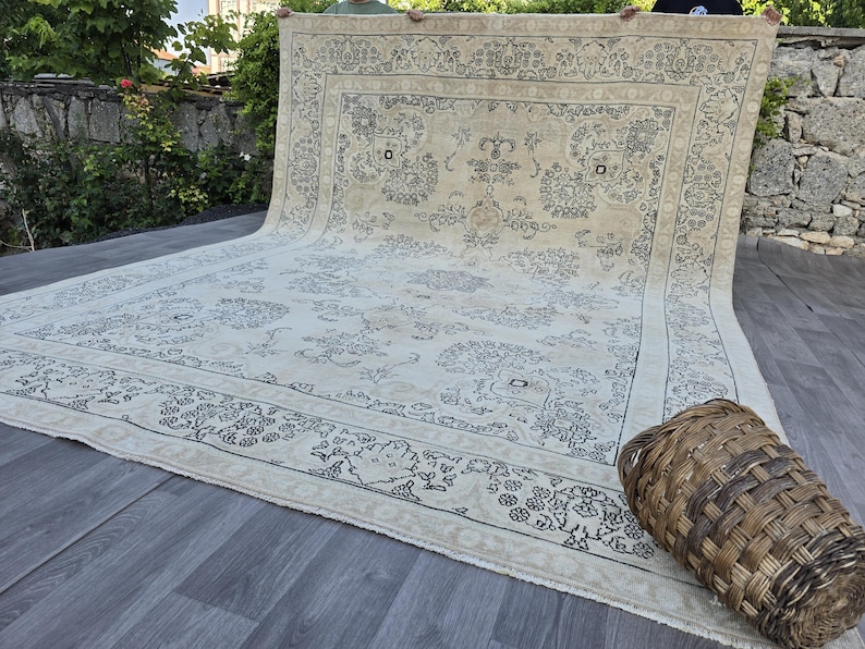 May include: A large rectangular area rug featuring a cream-colored base with intricate dark gray floral and vine patterns. The rug has a wide decorative border with repeating botanical motifs and a central medallion design, finished with fringe edges.