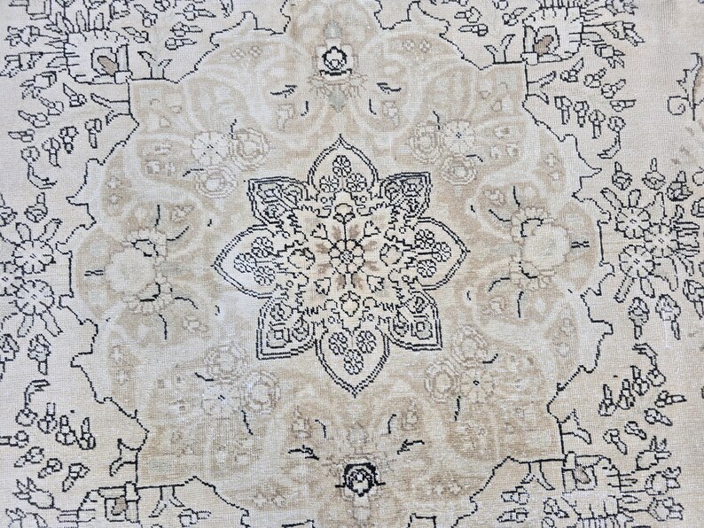 May include: A woven rug featuring a central beige floral medallion with intricate black line work. The design includes symmetrical botanical patterns and scrolling vines set against a light cream background, creating a detailed textile surface.
