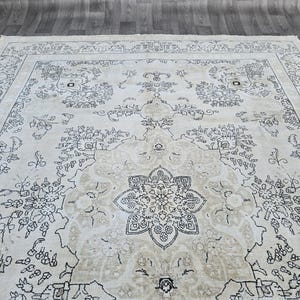 May include: A large area rug featuring a cream-colored background with intricate dark gray floral and botanical patterns. The design includes a central medallion surrounded by symmetrical vine motifs and a detailed border with repeating floral elements.