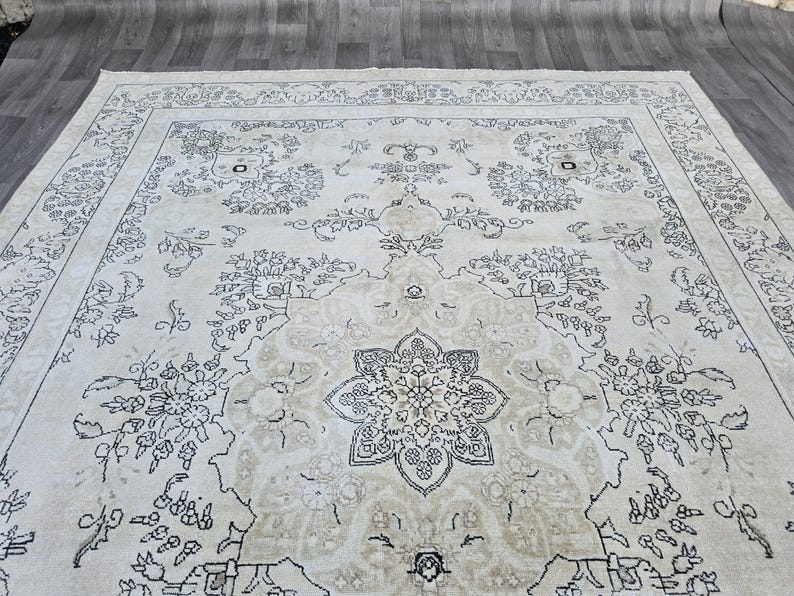 May include: A large area rug featuring a cream-colored background with intricate dark gray floral and botanical patterns. The design includes a central medallion surrounded by symmetrical vine motifs and a detailed border with repeating floral elements.