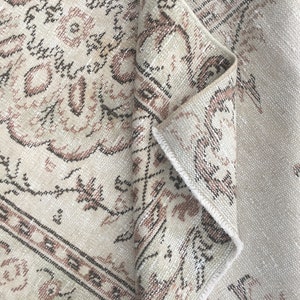 Puede incluir: Una alfombra beige con un patrón floral marrón y rosa. La alfombra está doblada por la mitad, mostrando el lado de atrás.