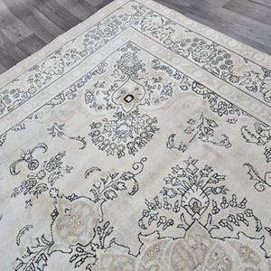 May include: A large area rug featuring a cream-colored background with intricate black floral and botanical line-art patterns. The design includes a wide decorative border with repeating flower motifs and a central field with symmetrical floral arrangements.