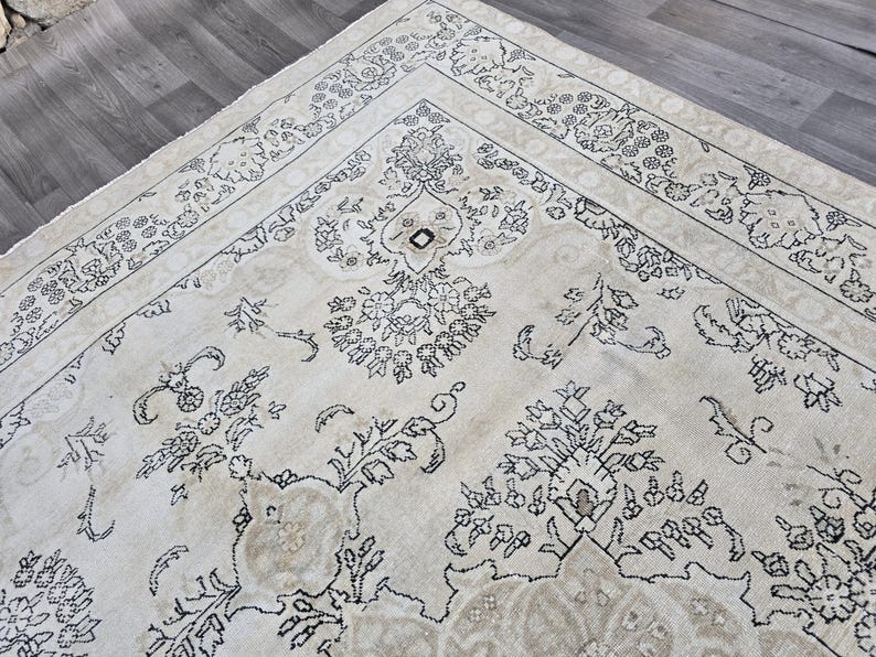 May include: A large area rug featuring a cream-colored background with intricate black floral and botanical line-art patterns. The design includes a wide decorative border with repeating flower motifs and a central field with symmetrical floral arrangements.