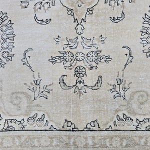 May include: A woven rug featuring a light beige background with intricate black and grey floral and botanical patterns. The design includes symmetrical circular motifs, stylized leaves, and scrolling vines across the surface of the textile.