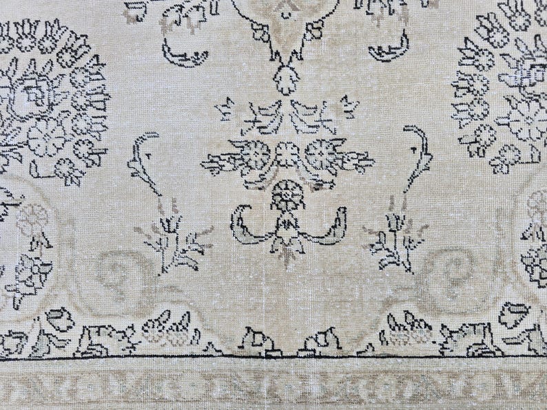 May include: A woven rug featuring a light beige background with intricate black and grey floral and botanical patterns. The design includes symmetrical circular motifs, stylized leaves, and scrolling vines across the surface of the textile.