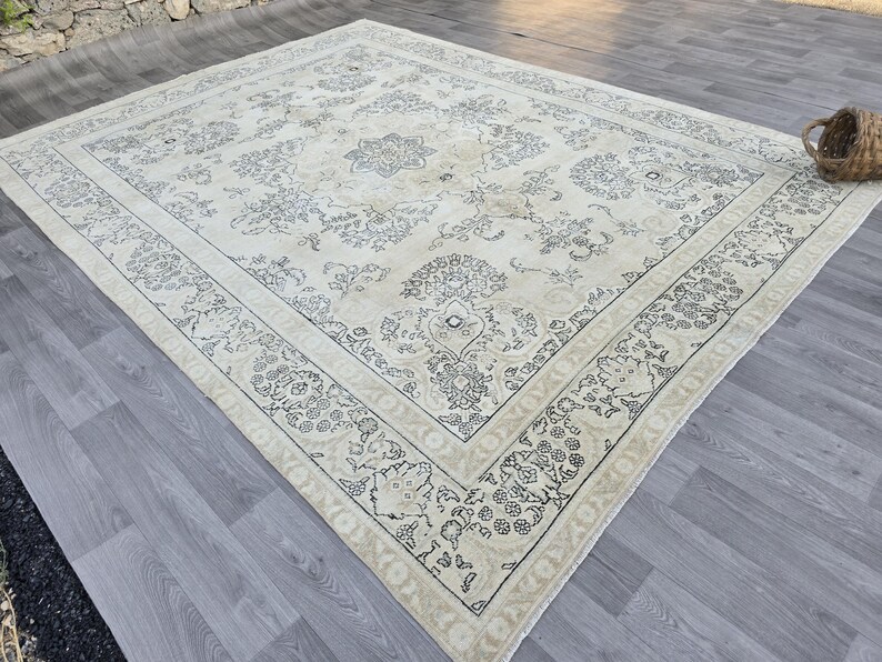 May include: A large rectangular area rug featuring a cream-colored base with intricate dark gray floral and vine patterns. The design includes a central medallion and a wide decorative border with repeating botanical motifs and a fringed edge.