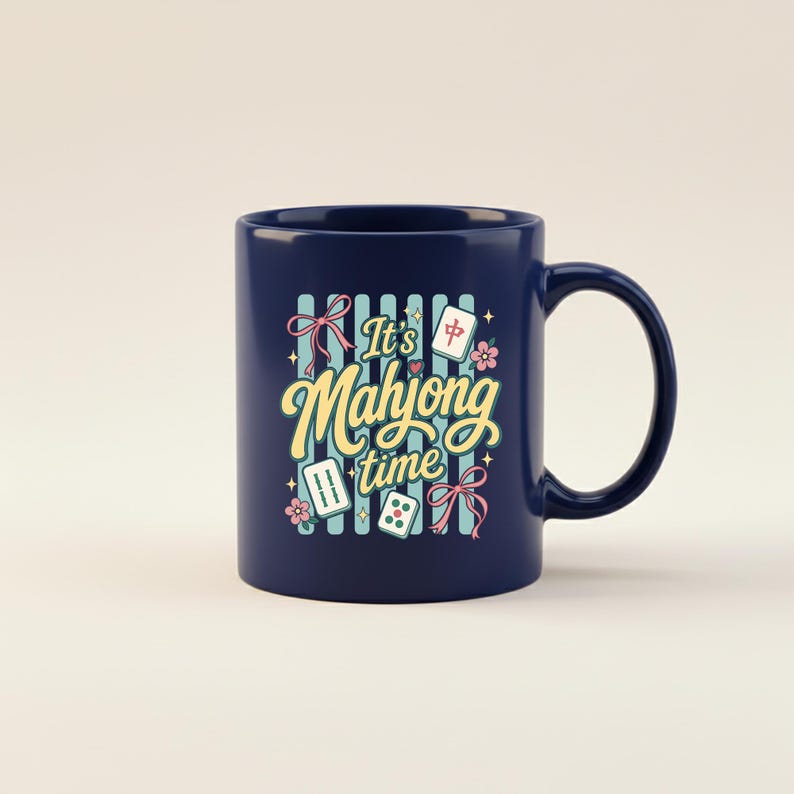 Puede incluir: Taza de cer&aacute;mica azul marino con asa. La taza presenta el texto "It's Mahjong time" en una fuente caprichosa, junto con ilustraciones de fichas de mahjong, flores y lazos. El fondo tiene rayas azules verticales.