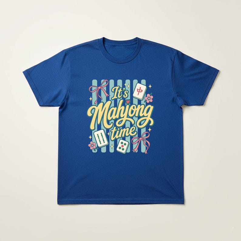 Puede incluir: Camiseta azul real con la frase "It's Mahjong Time" en escritura amarilla. El dise&ntilde;o incluye lazos rosas, flores y fichas de Mahjong. La camiseta tiene mangas cortas y cuello redondo.