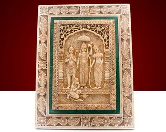 Pode incluir: Uma placa de parede decorativa com uma imagem esculpida de uma divindade hindu com duas figuras em pé de cada lado. A placa é emoldurada com uma borda verde e dourada.