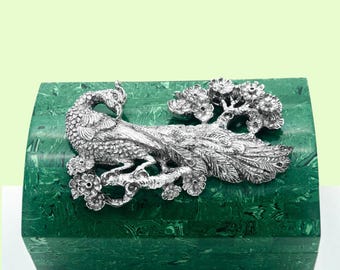 May include: A green malachite box with a silver peacock design on the lid. The peacock is perched on a branch with flowers.