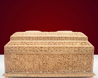 May include: A wooden box with intricate floral carvings. The box is light brown in colour and has a rectangular shape. The box has a hinged lid and sits on four small feet.