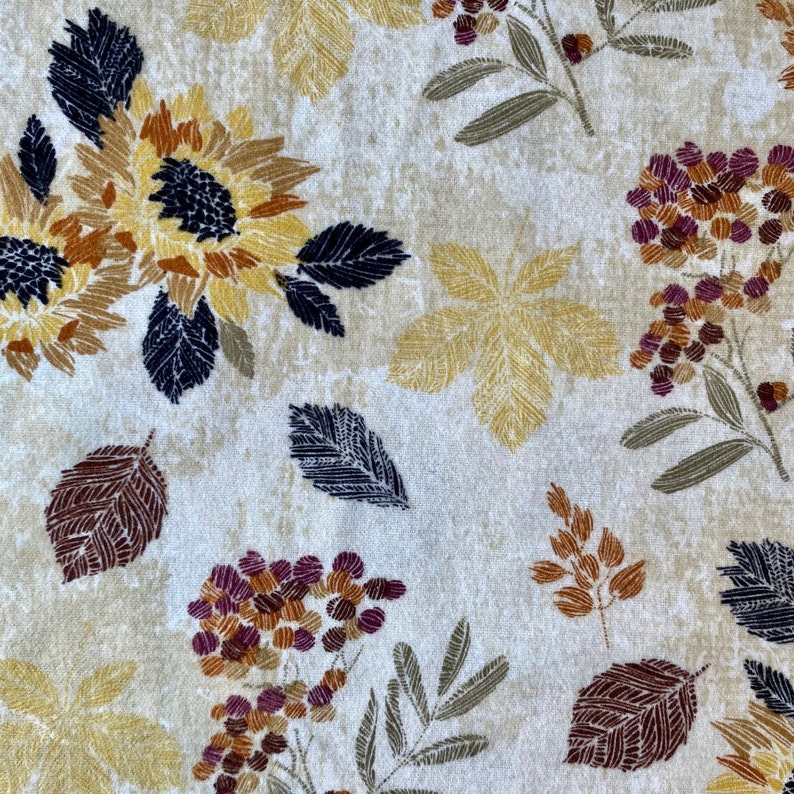 May include: A cream-colored fabric with a repeating pattern of sunflowers, leaves, and floral elements in shades of yellow, brown, and burgundy. The design includes detailed leaf and flower illustrations.