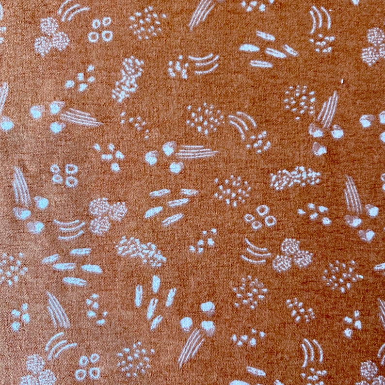 May include: Close-up of a textured, rust-colored fabric with a repeating pattern of white abstract shapes. The design includes small dots, curved lines, and clusters of dots, creating a visually interesting surface.