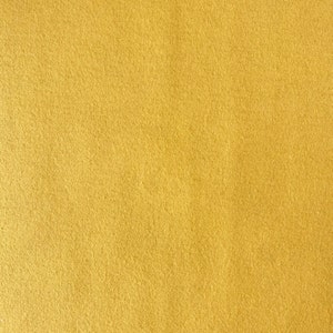 May include: Close-up of a solid, textured fabric in a warm, golden-yellow hue. The material has a slightly fuzzy appearance, suggesting a soft texture. The color is consistent across the entire surface, with subtle variations in tone.